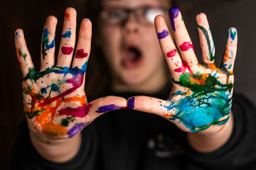  A child looks happy or surprised as her hands are covered in red, pink, yellow, orange, red, blue, green, and purple ink.  Concepts: art, education, play, watercolor, joy, mess, creativity, fun, enjo