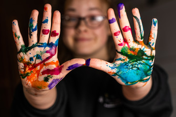  A child looks happy or surprised as her hands are covered in red, pink, yellow, orange, red, blue, green, and purple ink.  Concepts: art, education, play, watercolor, joy, mess, creativity, fun, enjo