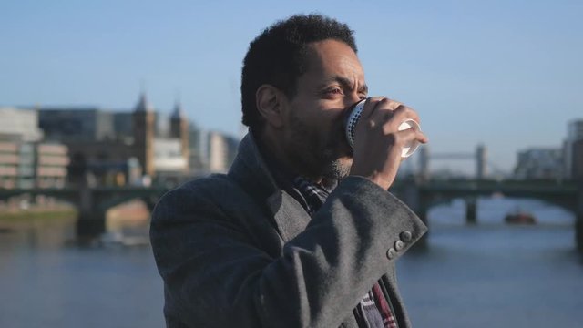 African man drinks a cup of coffee at River Thames in London