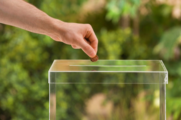 Man putting coins into donation box on blurred background, closeup
