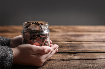 Woman holding donation jar with coins at wooden table, closeup. Space for text