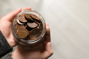 Woman holding donation jar with coins on light background, top view. Space for text
