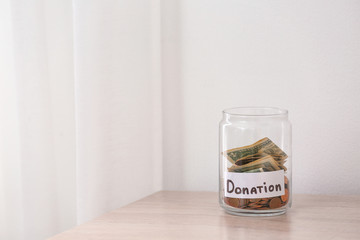 Glass jar with money and label DONATION on table against light background. Space for text