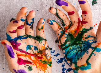 A child's hands are covered in red, pink, yellow, orange, red, blue, green, and purple ink.  Concepts: art, education, play, watercolor, finger painting, mess, creativity, fun, enjoyment