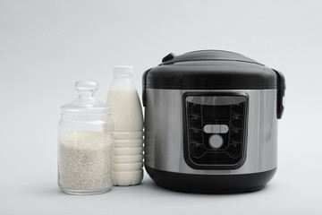 Modern electric multi cooker, rice and milk on grey background