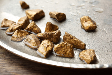 Plate with gold nuggets and water on table, closeup