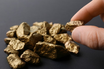 Man taking gold nugget from pile on dark background, closeup