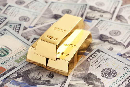 Shiny gold bars on pile of dollar bills