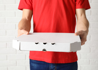Young man with pizza box near white brick wall. Food delivery service