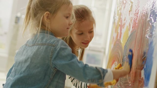 Two Happy Little Girls with Hands Dipped in Colorful Paint Put Handprints and Draw Abstractions on the Wall. They are Having Fun and Laugh. Home is Being Renovated.
