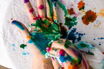  A child cleans up hands that are covered in red, pink, yellow, orange, red, blue, green, and purple ink.  Concepts: art, education, play, watercolor, finger painting, mess, creativity, fun, enjoyment