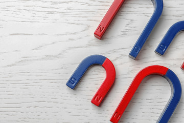 Red and blue horseshoe magnets on wooden background, top view with space for text