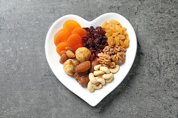 Heart shaped plate with different dried fruits and nuts on table, top view