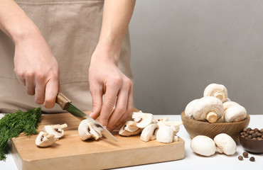 Obraz na płótnie Canvas Young woman cutting fresh champignon mushrooms on wooden board, closeup view. Space for text