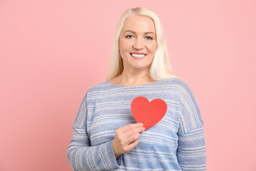 Portrait of mature woman with decorative paper heart on color background