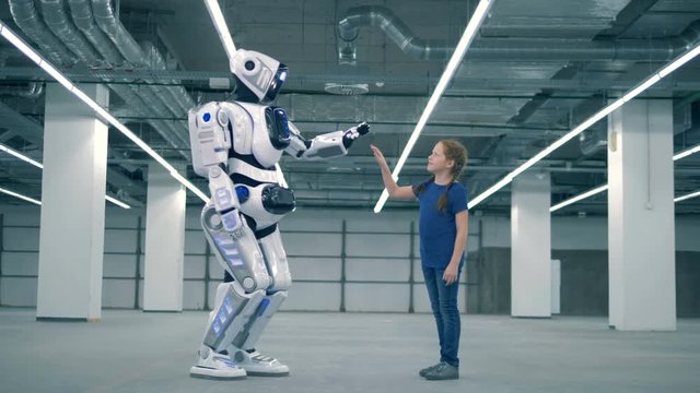 Human-like robot is giving a high-five to a little girl