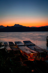 Amazing sunset in luang prabang over the mekong river. Tourist and house boats in the water. Sky is...
