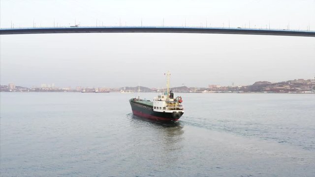 Aerial view of trading ship floating under Russian bridge. Vladivostok, Russia
