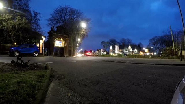 Timelapse view of town intersection traffic, slower moving vehicles entering archway to church.