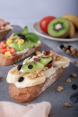 Sandwiches with banana, kiwi, grains and mayonnaise on gray board as background