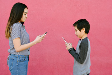 A brother and sister text to each other on smart phones while being withing distance from one...