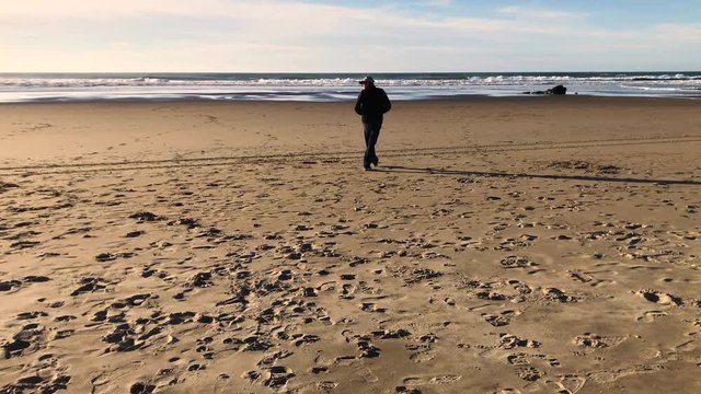 Lonely man walking on a beautiful beach in Bandon, Oregon during daytime, looking out on the ocean