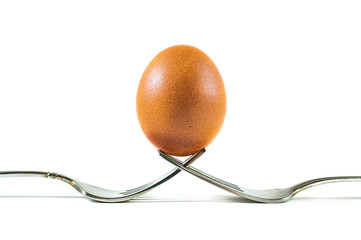 A brown organic egg balanced on two forks isolated on a white background.