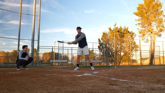 A baseball player ducking to avoid getting hit by a wild pitch during an amateur game in the park at sunset  SLOW MOTION.