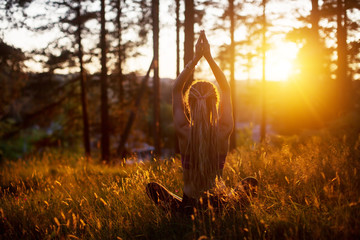 Silhouette of Young female wearing long hair dreadlocks seating in forest outdoor, doing yoga...