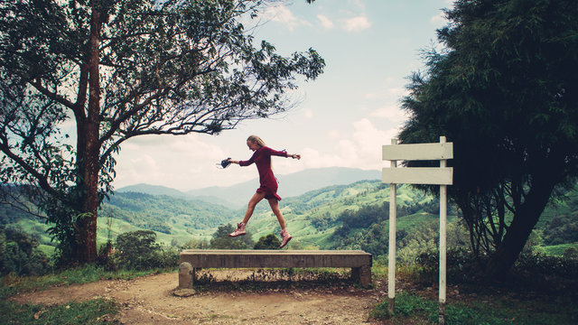 Young female enjoy, jumping on tea plantations mountains view point with camera in her hand