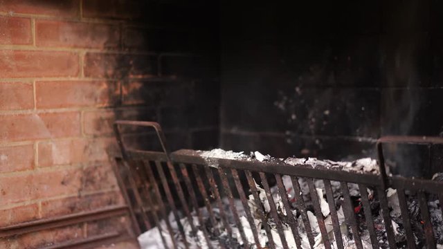 Brick fireplace full of ashes and smoke from burnt wooden branches. Close-up, 4K shoot