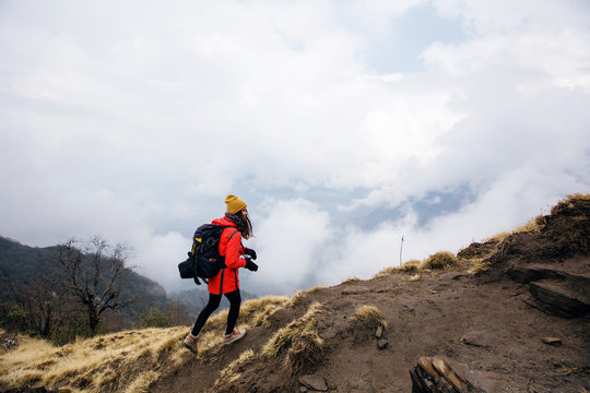 Young traveller woman wearing backpack, red jacket and black hat walking  in fog mountain trekking with photo camera
