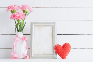 Valentines day and love concept. Pink carnation flower in vase with old vintage picture frame and red heart and on white background.