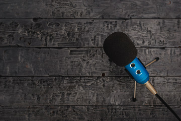 Blue microphone with black wire on black wooden table. Equipment for conferences, music studios and meetings.