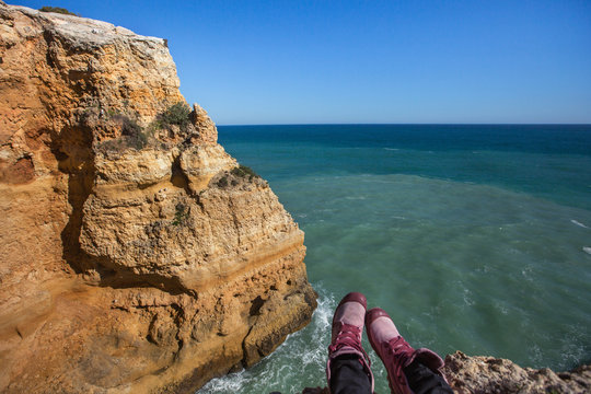 Traveler feet wearing pink shoes above ocean cliff