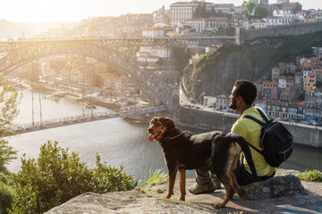 Traveler man with dog enjoying city view in Porto, famous iron bridge and Douro rive on background