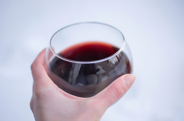 Glass of red wine in female hand on blurred white snow background.