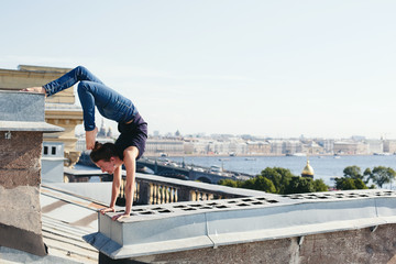 Young female doing yoga, standing on her hands on roof top in city center