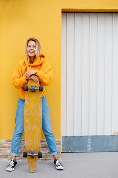 Street portrait of positive young female wearing orange hoody riding with skateboard in city