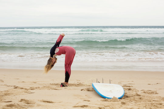 Happy funny positive female surfer with surf board on ocean beach doing exercises
