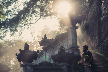 Man seating in misty Bali temple. Fog and beautiful sunlight