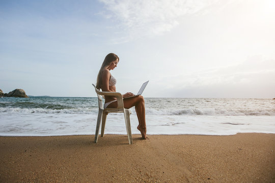 Young woman working on laptop seating on office chair on tropical beach