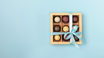 Various chocolates in crafting paper box with a satin blue ribbon on a bright blue background. Flat...