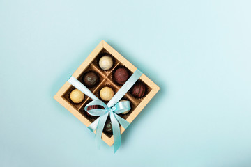 Various chocolates in crafting paper box with a satin blue ribbon on a bright blue background. Flat lay. Copy space
