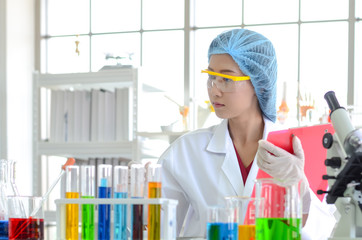 The woman scientist in laboratory doing experiments with chemical liquid and doing checklist and record data from testing in the lab.