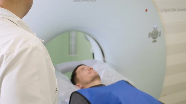 Male patient is moving into a CT-scanner. Medical equipment: computed tomography machine in diagnostic clinic. Health concept. Doctor presses settings button of CT MRI scanner. hd
