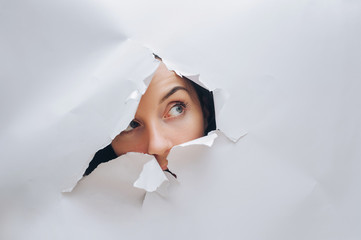 A girl with a cunning expression. Portrait of a woman looking through the hole in white paper....