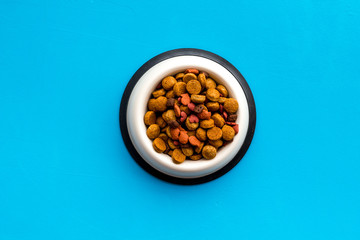 Dry dog food in bowl on blue backgorund top view copy space