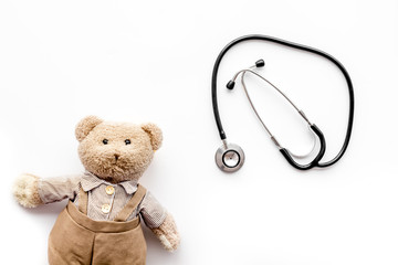 Children's doctor concept. Teddy bear toy and stethoscope on white background top view copy space