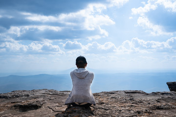 Naklejka premium A person sitting on rocky mountain looking out at scenic natural view and beautiful blue sky